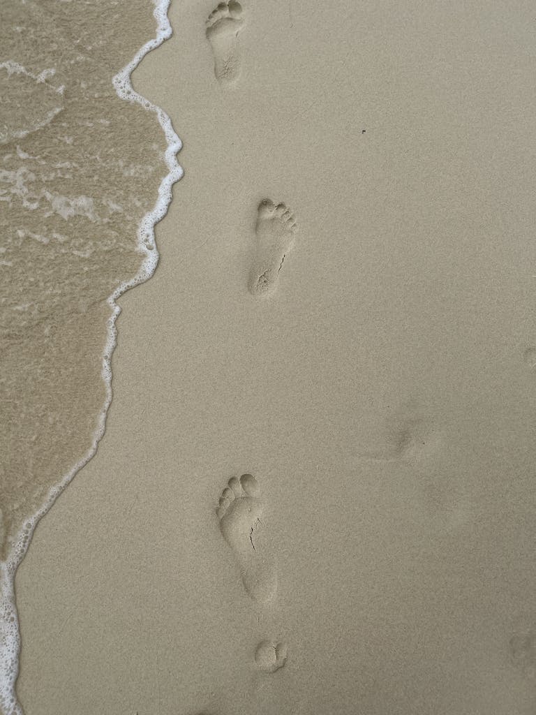 Footprints in soft sand by ocean waves, capturing a serene beach moment.