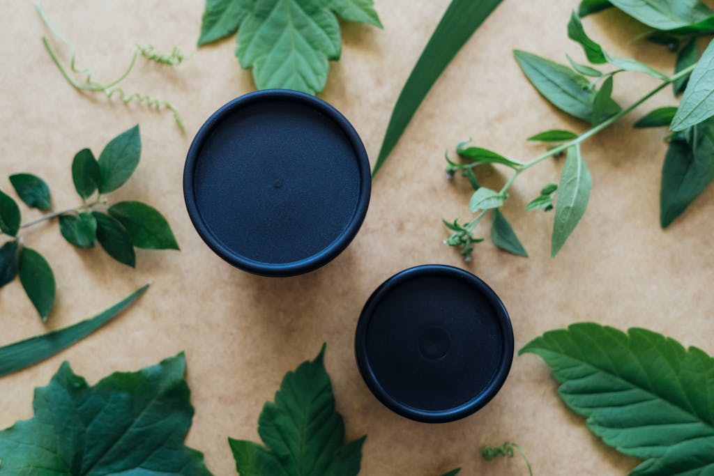 Top view of herbal leaves and black containers on a beige background.